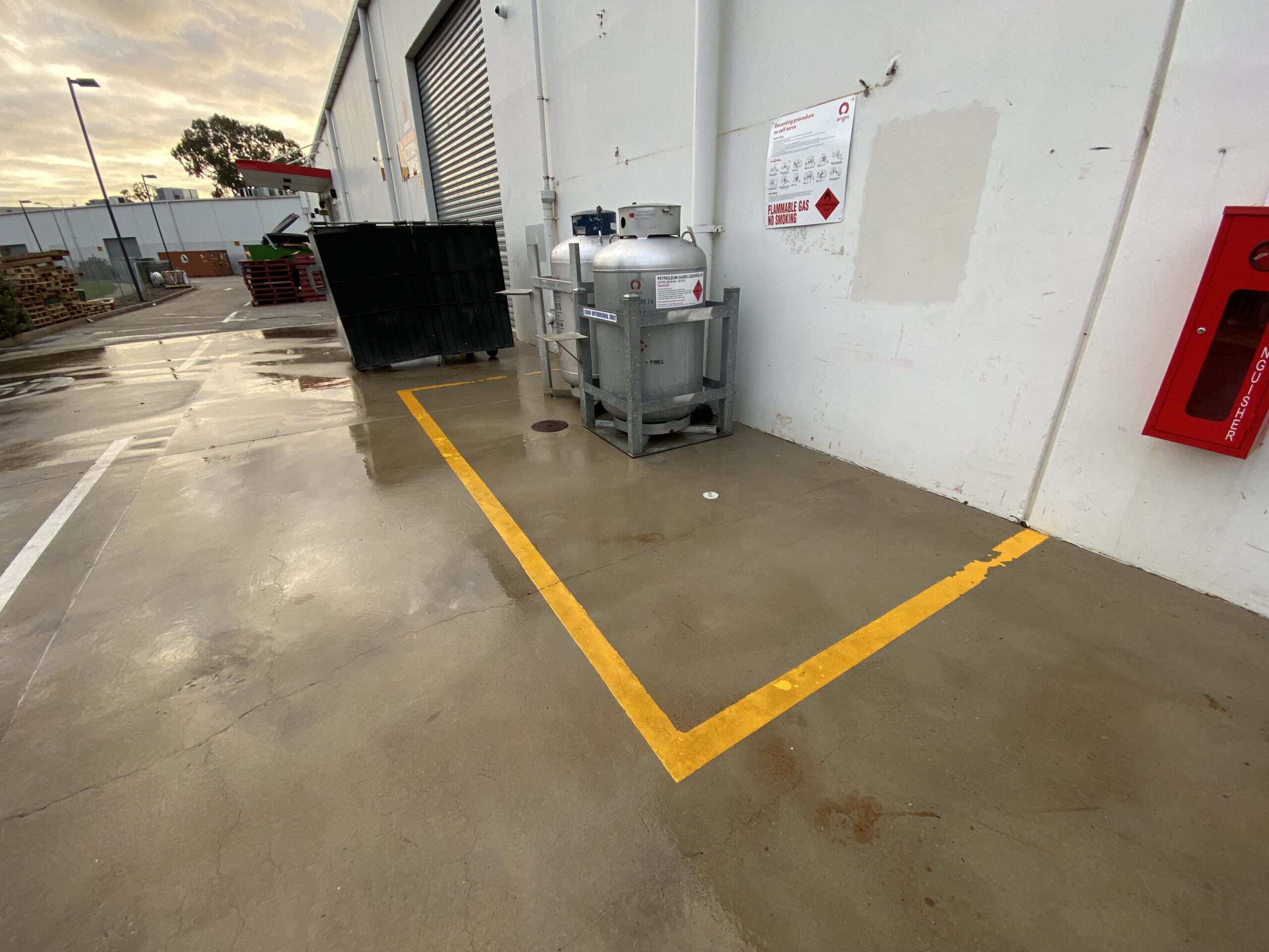 Warehouse floor with marked yellow lines and industrial equipment outside.