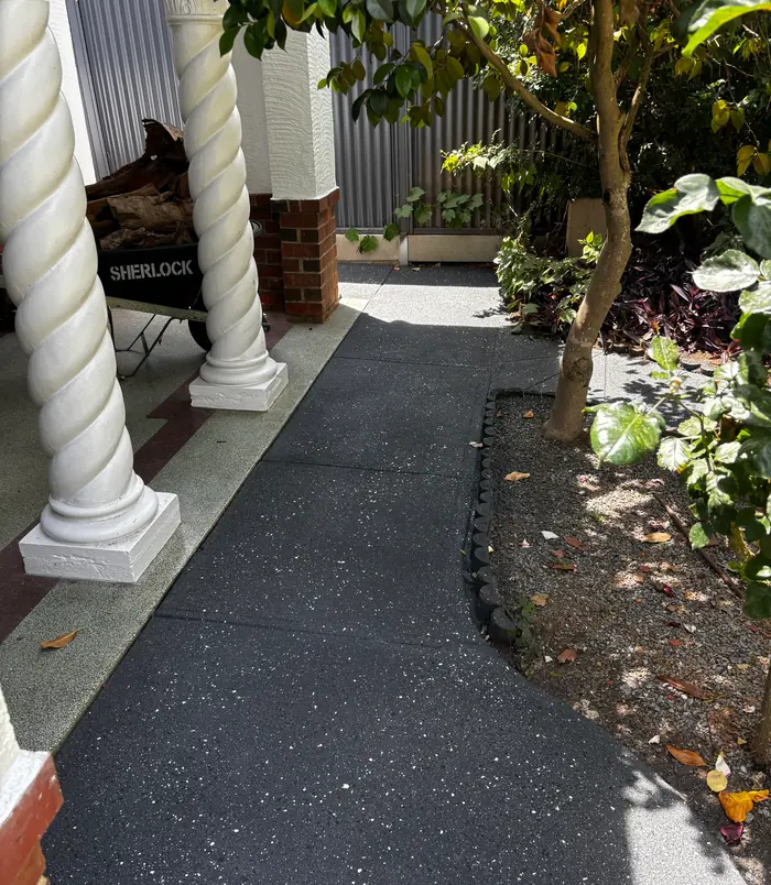 Dark grey resurfaced concrete path beside white twisted veranda posts and a garden