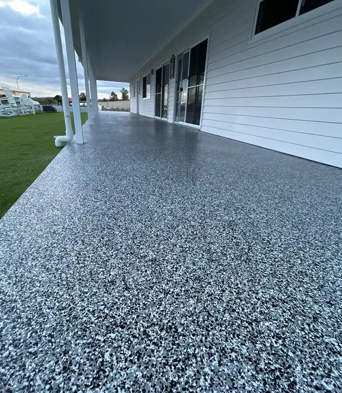 Blue-grey speckled epoxy flake veranda floor beside a white weatherboard house and lawn