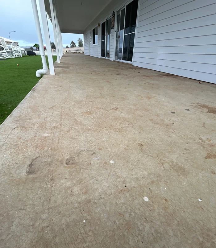 Rough, unsealed concrete veranda floor beside a white weatherboard house and lawn, before epoxy flooring