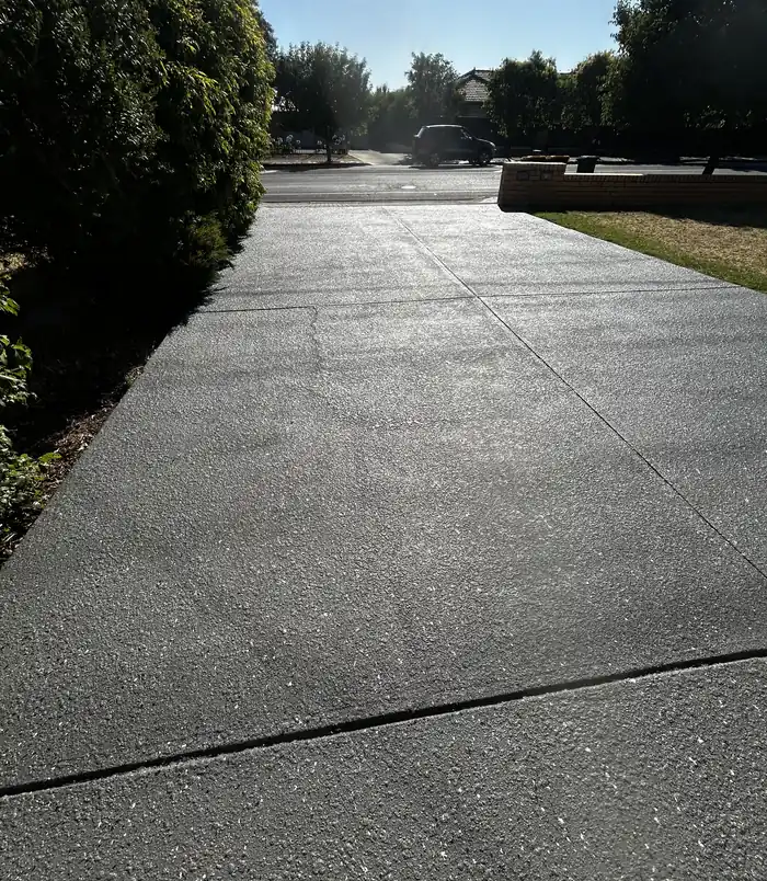 Smooth dark grey resurfaced concrete driveway beside a lawn