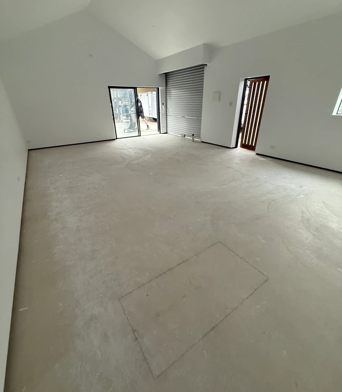 Bare concrete floor in an empty room with glass doors and a roller shutter, before epoxy flooring