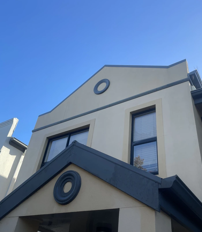 Clean rendered house facade with a round window under a blue sky after pressure washing
