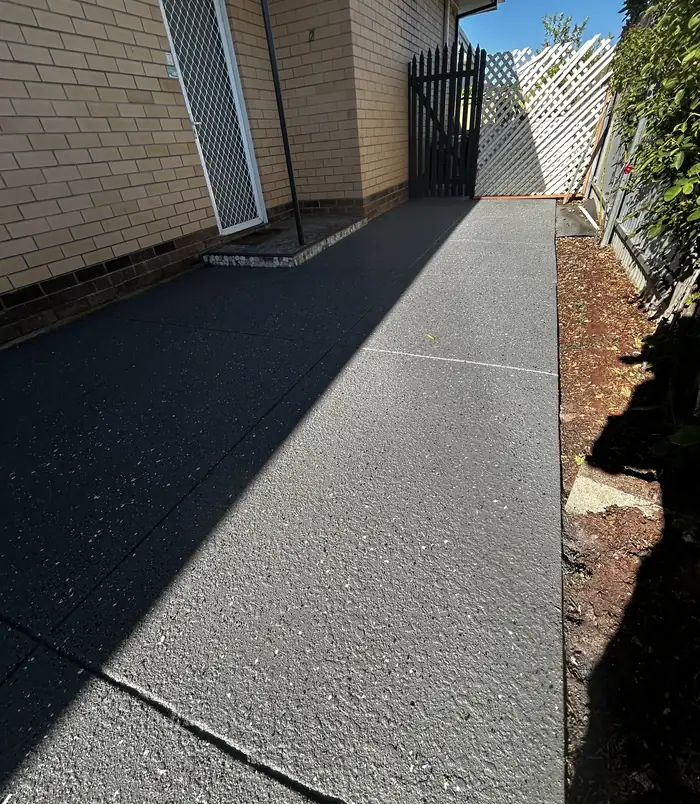 Dark speckled resurfaced concrete side path beside a brick wall and gate