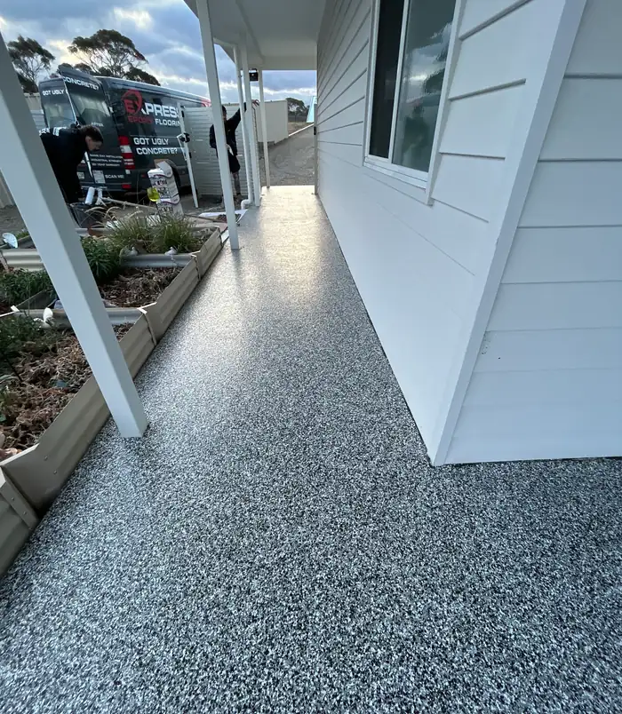 Speckled epoxy flake veranda floor beside a white weatherboard wall with a parked car beyond