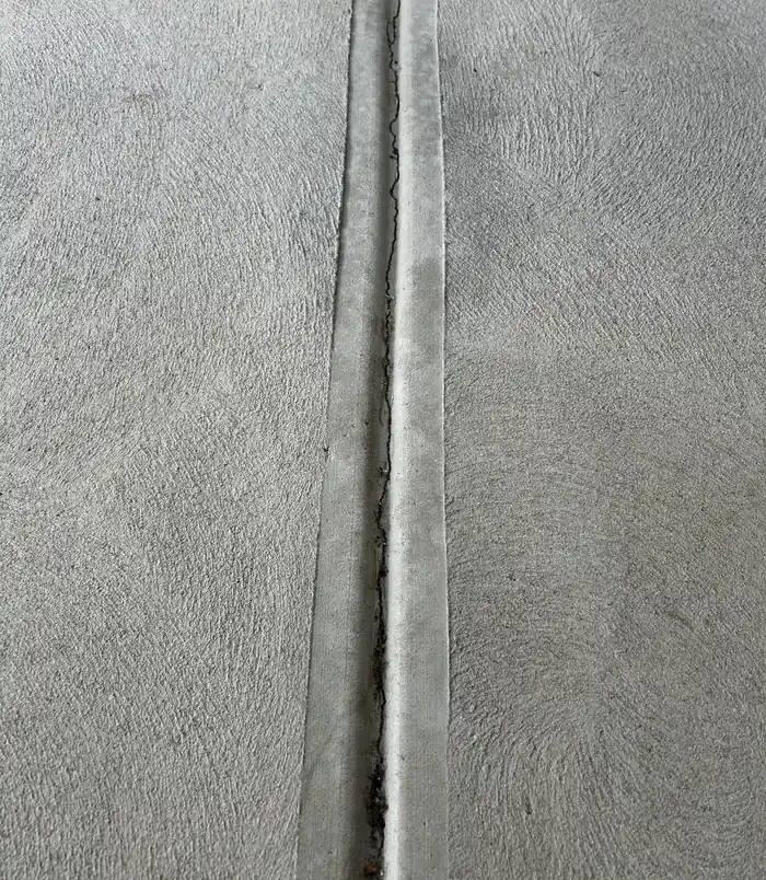 Close-up of cracked, worn concrete with a joint line, before concrete resurfacing