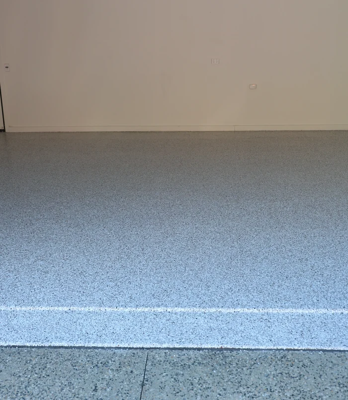Close view of a blue-grey speckled epoxy flake floor against a cream wall