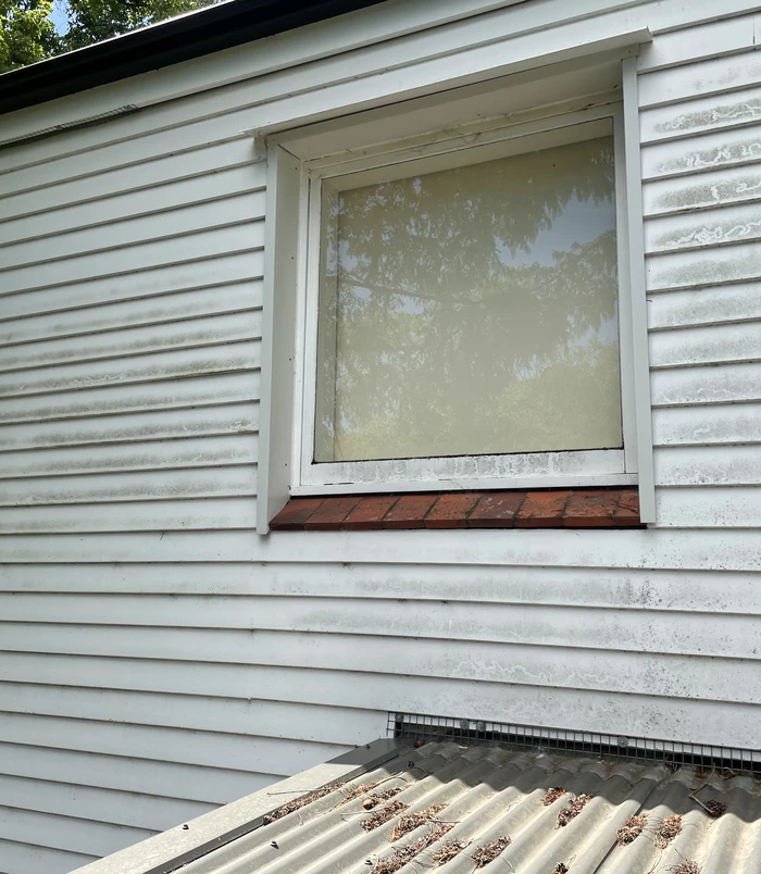 Weatherboard wall with a window, dirty and streaked with grime, before pressure washing