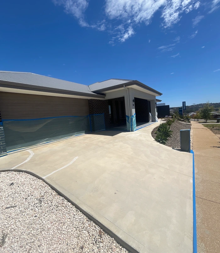 Concrete driveway masked with blue tape in front of a modern home, before resurfacing