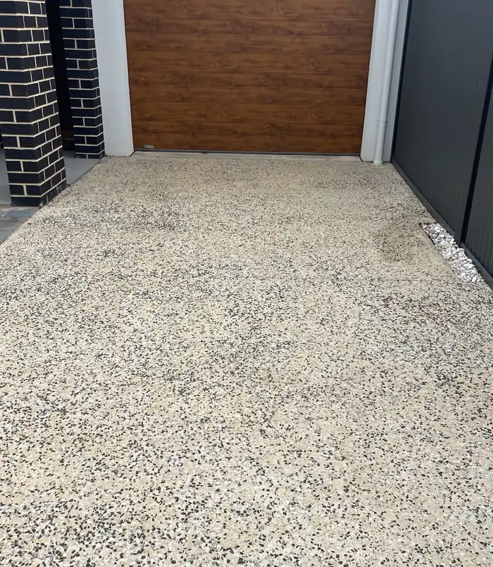 Clean, light exposed aggregate driveway in front of a timber-look garage door after pressure washing