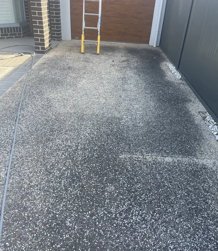 Dark, dirty exposed aggregate driveway in front of a garage, before pressure washing