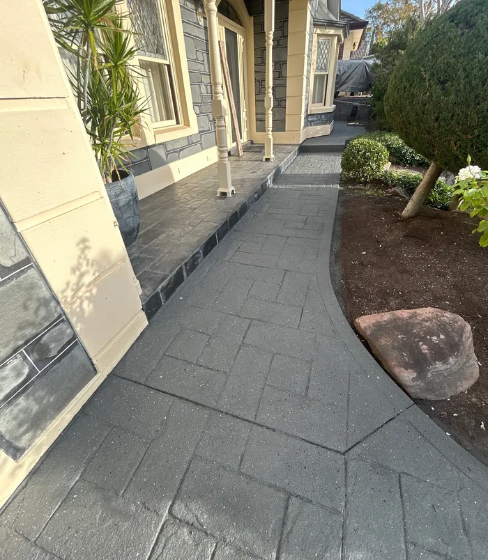 Smooth grey resurfaced concrete path beside a heritage home and garden