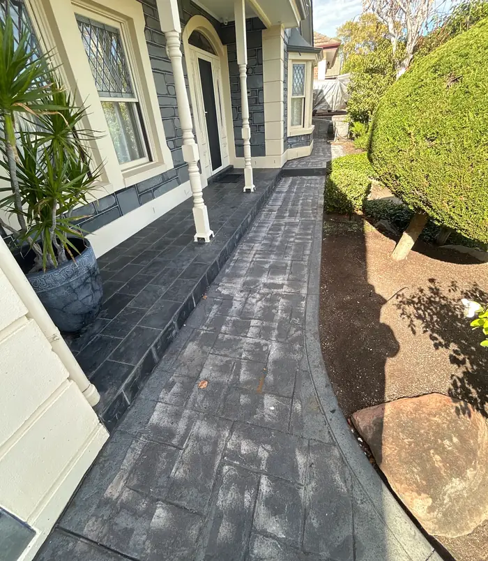 Dark, stamped-pattern concrete path beside a heritage home and garden, before concrete resurfacing