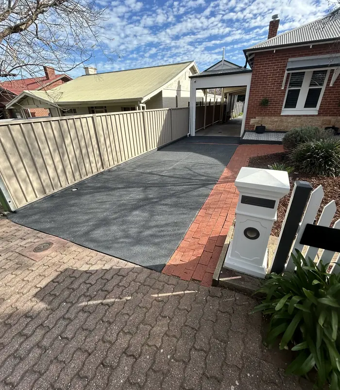 Dark grey resurfaced concrete driveway leading to a character home with a front garden