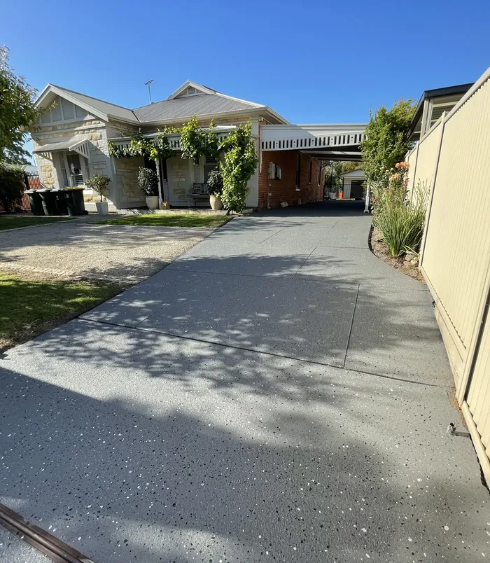 Dark grey resurfaced concrete driveway leading to a character home with a front garden