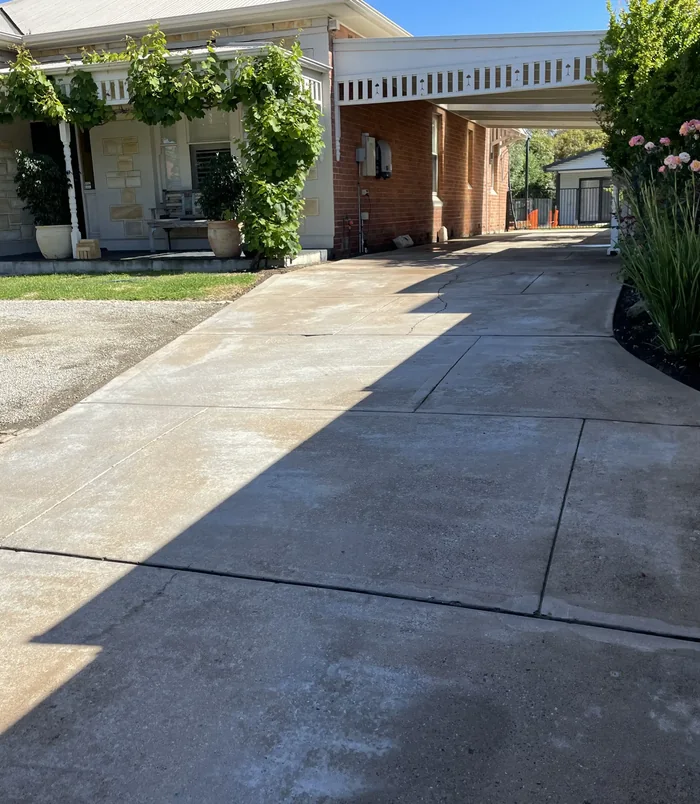 Pale, weathered concrete driveway curving toward a carport and cottage, before concrete resurfacing