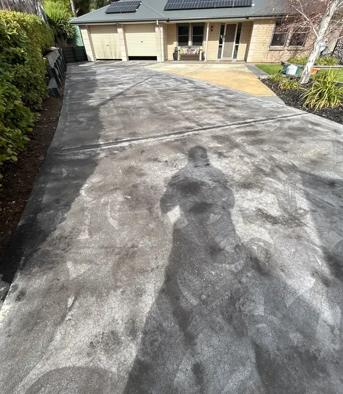 Stained, scuffed concrete driveway with footprints leading to a garage, before concrete resurfacing