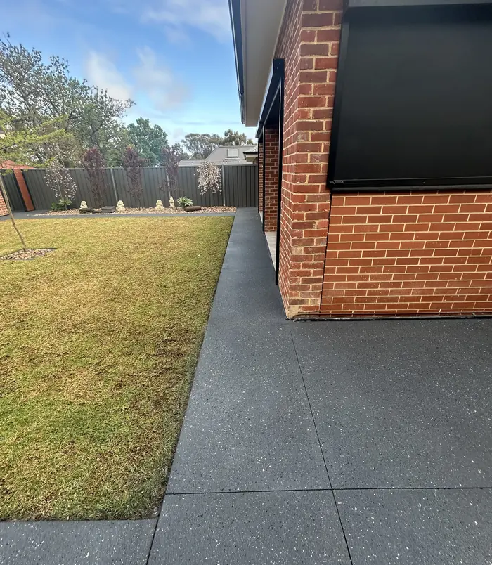 Smooth dark grey resurfaced concrete path beside a red brick wall and lawn
