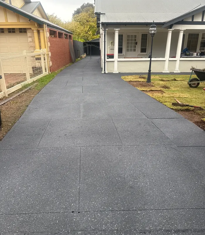 Long dark grey resurfaced concrete driveway leading to a character home with a veranda