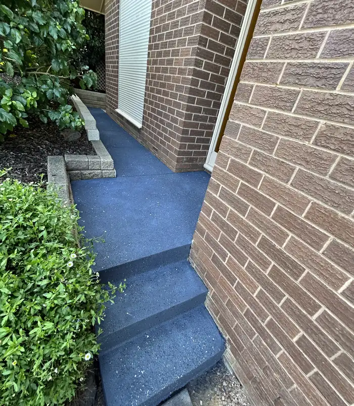 Blue-grey resurfaced concrete path beside a brick wall and garden bed