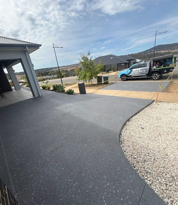 Dark grey resurfaced concrete driveway beside a carport with a work ute in the background