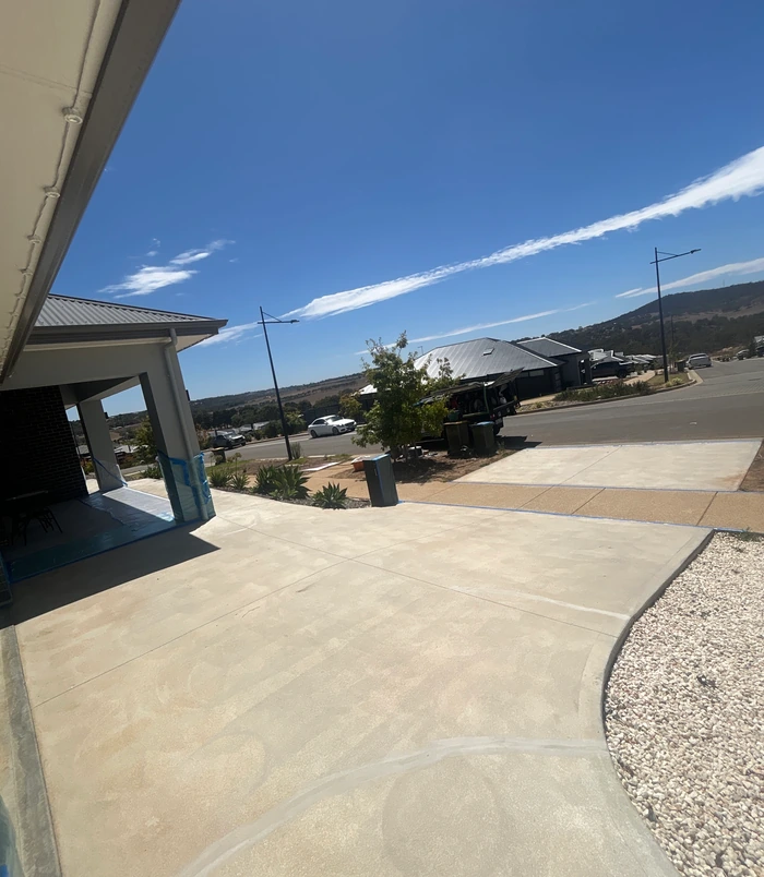 Pale, rough concrete driveway beside a carport with hills in the distance, before resurfacing