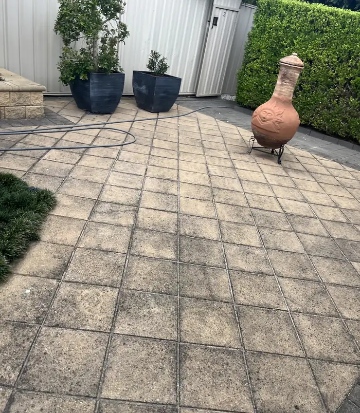 Grimy, discoloured patio pavers with a terracotta chiminea and planter pots, before pressure washing