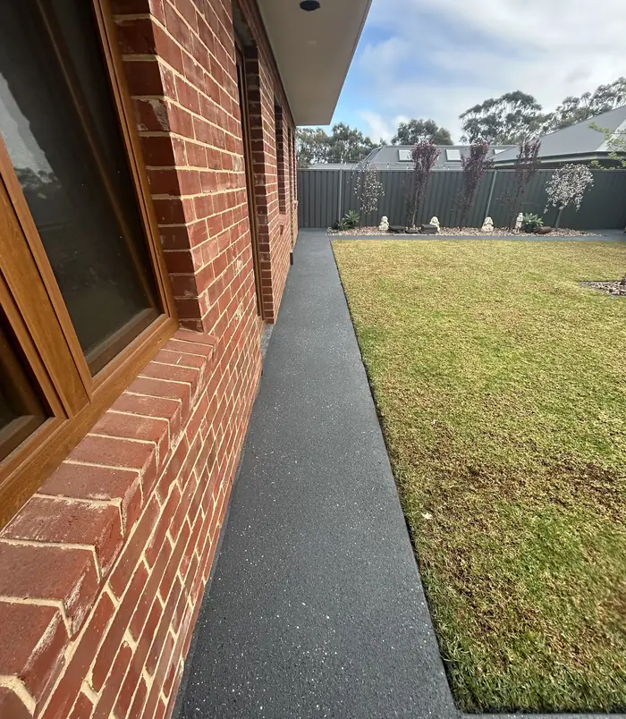 Dark grey resurfaced concrete path beside a red brick wall and lawn