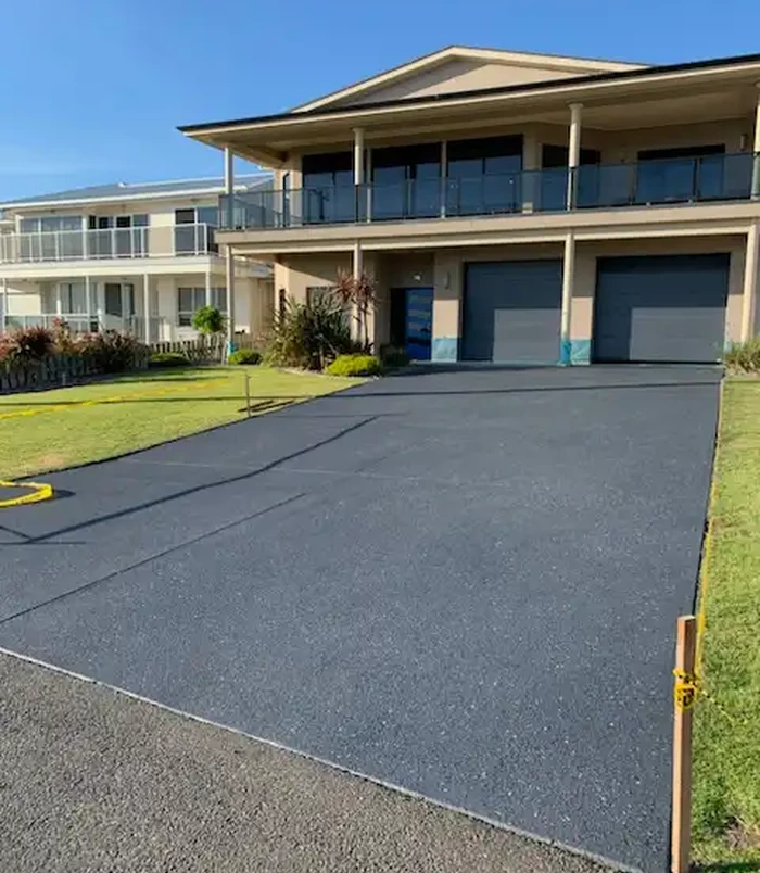Dark grey resurfaced concrete driveway leading to the garage of a two-storey home