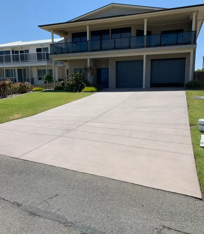 Pale, worn concrete driveway leading to the garage of a two-storey home, before resurfacing