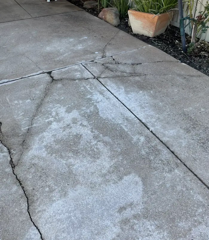 Cracked, patchy concrete slab beside garden pots, before concrete resurfacing