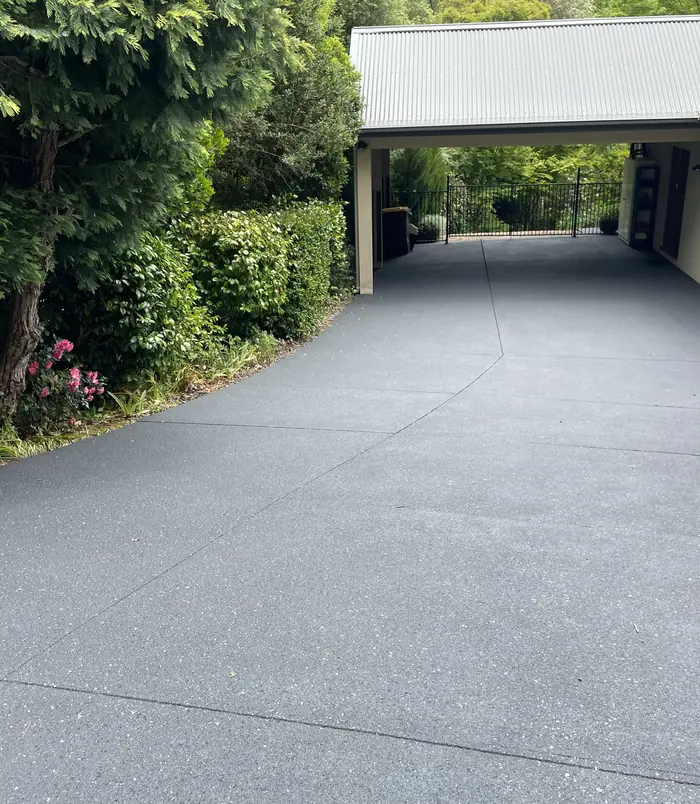 Dark grey resurfaced concrete driveway curving toward a carport beside a hedge