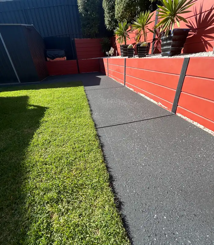 Dark resurfaced concrete path beside a red retaining wall and lawn
