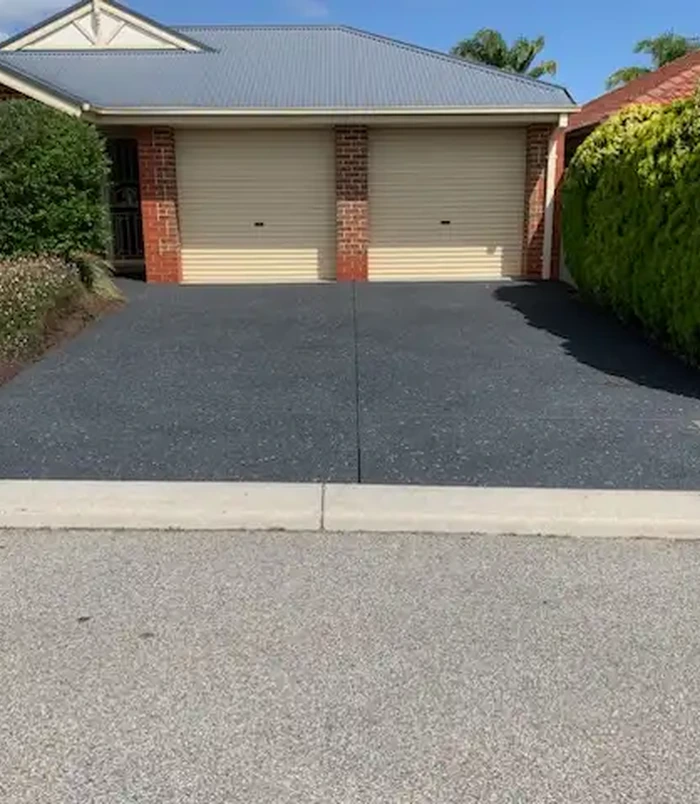 Dark resurfaced concrete driveway in front of a double garage with cream doors