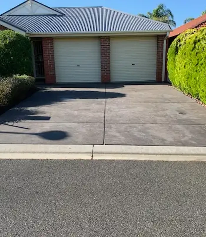 Faded concrete driveway in front of a double garage with cream doors, before concrete resurfacing