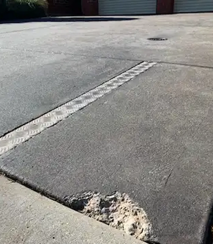 Worn grey concrete with a drainage strip across it, before concrete resurfacing