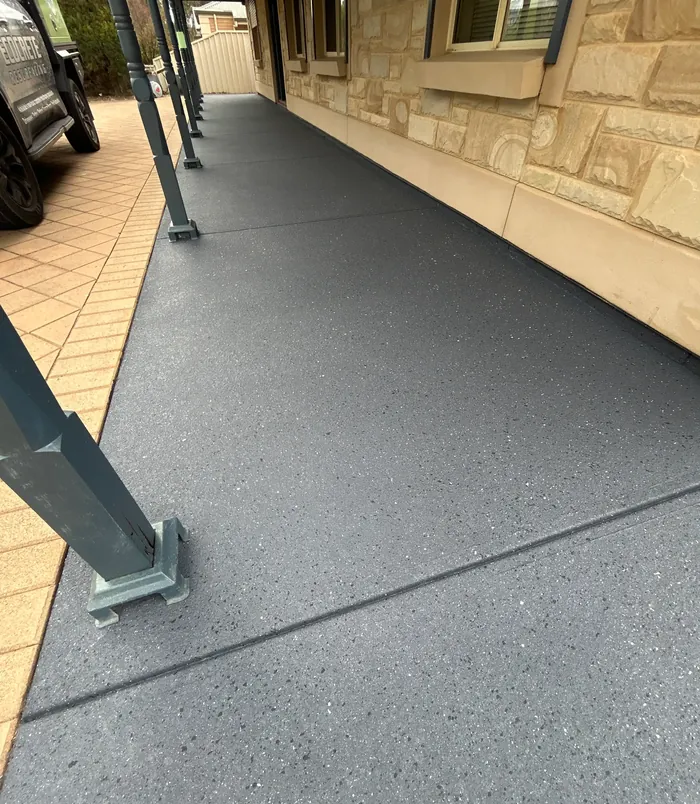 Dark grey resurfaced concrete path beside a sandstone wall and paved patio