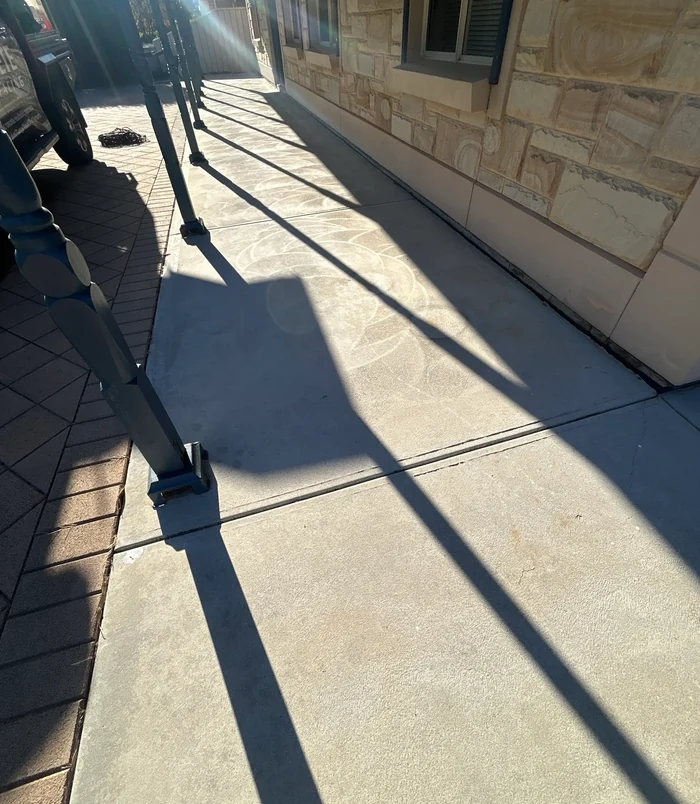 Stained concrete path beside a sandstone wall, before concrete resurfacing