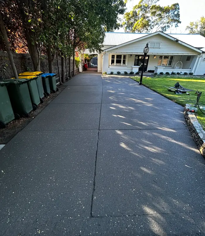 Long concrete driveway beside wheelie bins resurfaced with a clean, even grey finish