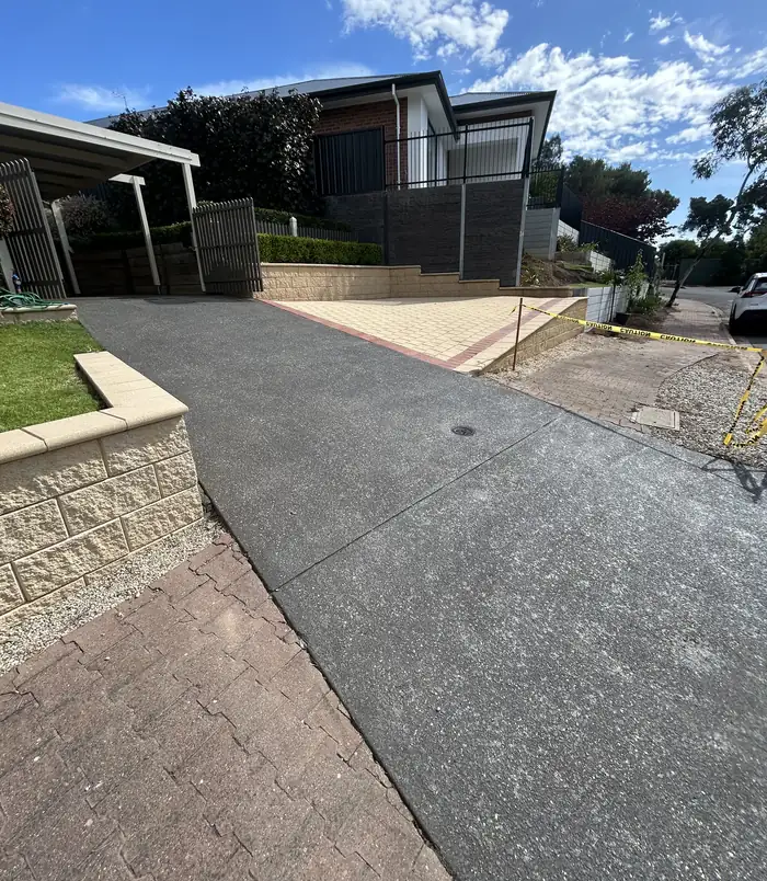 Dark grey resurfaced concrete driveway beside a stone retaining wall and modern home