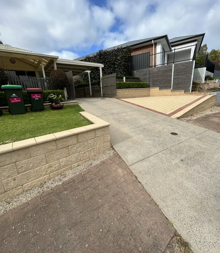 Pale, worn concrete driveway beside a lawn and modern home with a pergola, before resurfacing