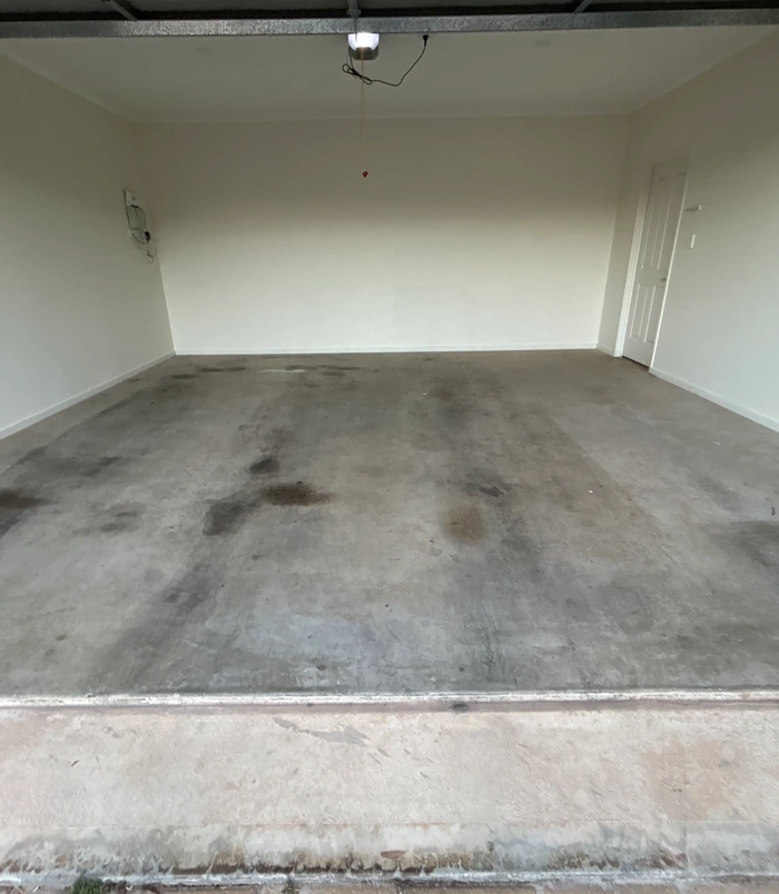 Empty garage with a stained, oil-marked concrete floor, before epoxy flooring