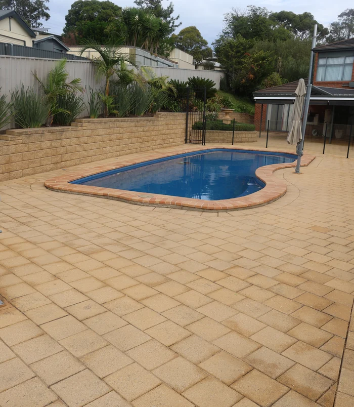 Clean, warm-toned brick pavers around a freeform blue swimming pool after pressure washing