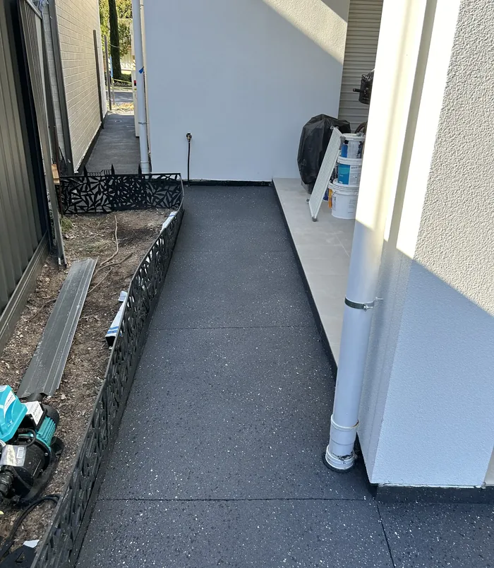 Narrow side path beside a white wall resurfaced in smooth dark grey concrete