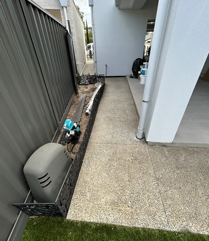 Narrow concrete side path beside a white wall, before resurfacing