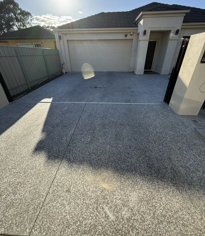 Stained, tired concrete driveway leading to a garage beside a grey fence, before concrete resurfacing
