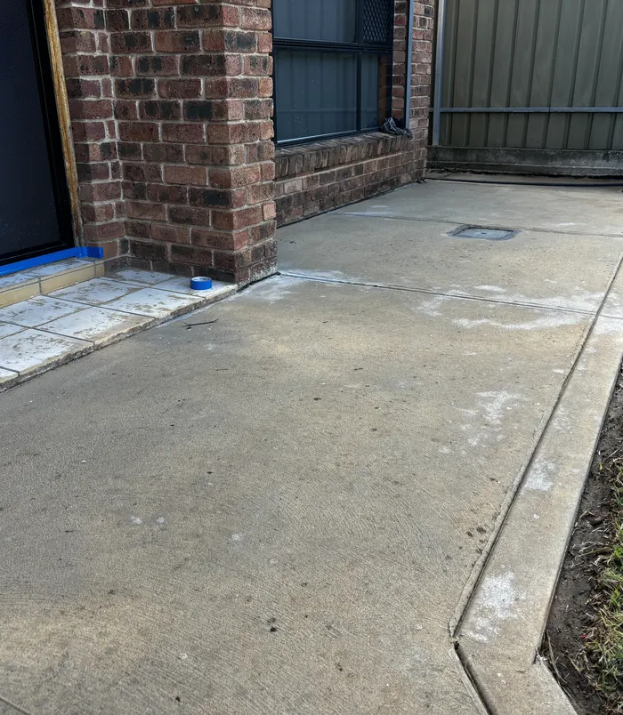 Worn concrete path beside a brick pillar with blue masking tape along the edge, before concrete resurfacing