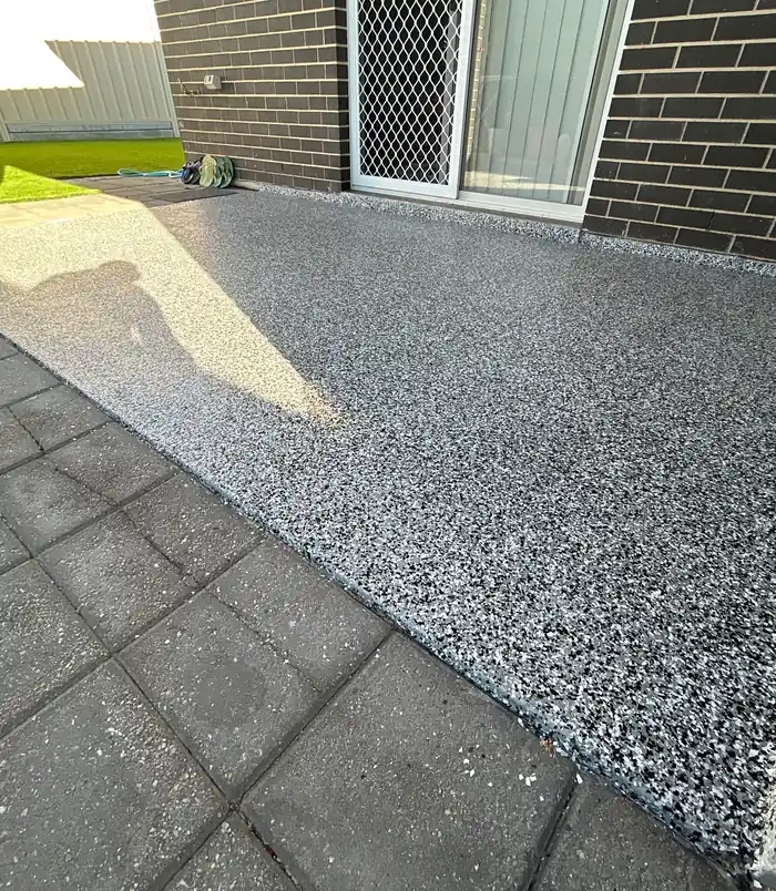 Grey speckled epoxy flake patio floor beside a dark brick wall and sliding door