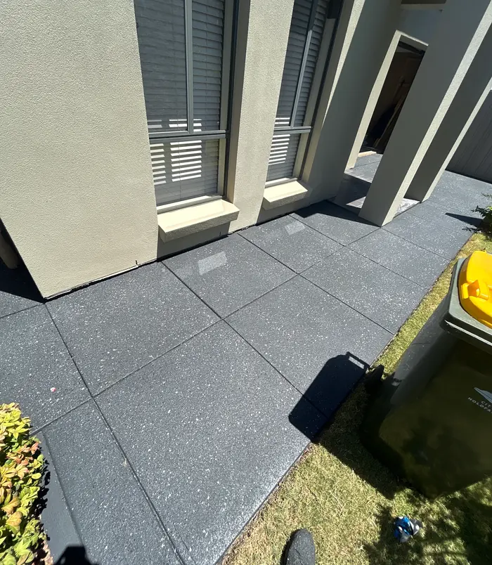 Dark grey resurfaced concrete patio beside a rendered wall with shuttered windows