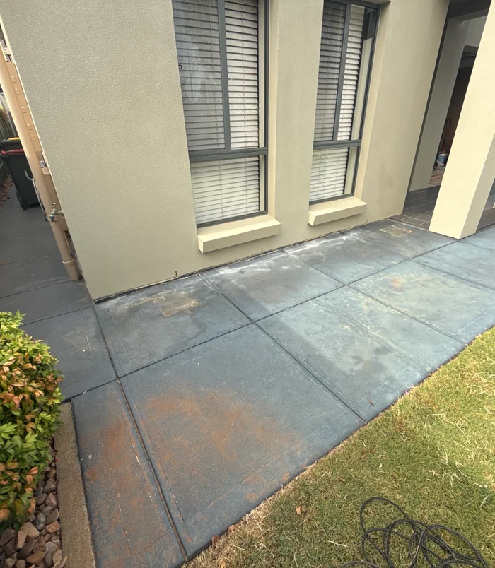 Stained, uneven concrete patio beside a rendered wall with shuttered windows, before resurfacing